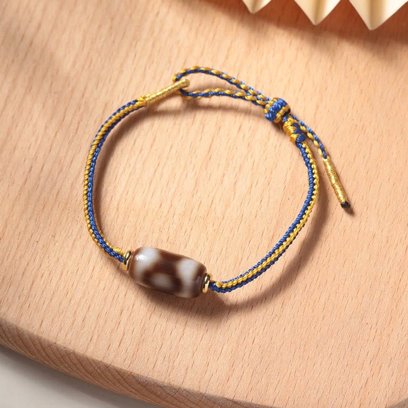 Tibetan three-eye Dzi bead bracelet in blue and gold, flat lay view showing complete adjustable design with sliding knot mechanism