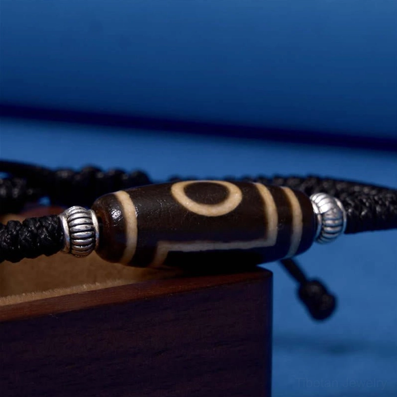 Three-eye dzi bead bracelet close-up showing silver alloy spacers and three-eye symbol protection meaning