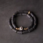 Three-eye dzi lava rock wrap bracelet flat lay - double wrap design with porous black volcanic beads and brass accents