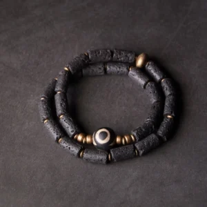 Three-eye dzi lava rock wrap bracelet flat lay - double wrap design with porous black volcanic beads and brass accents