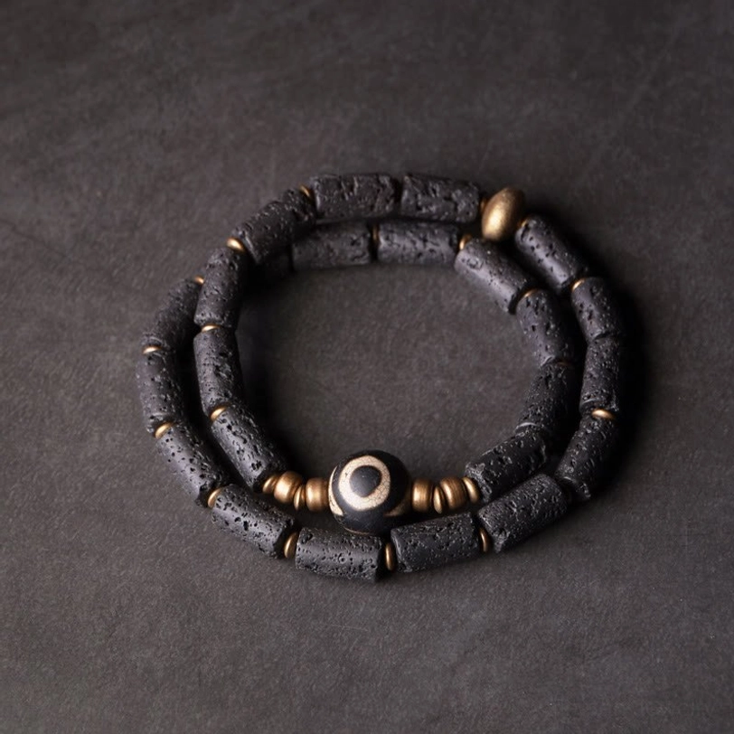 Three-eye dzi lava rock wrap bracelet flat lay - double wrap design with porous black volcanic beads and brass accents