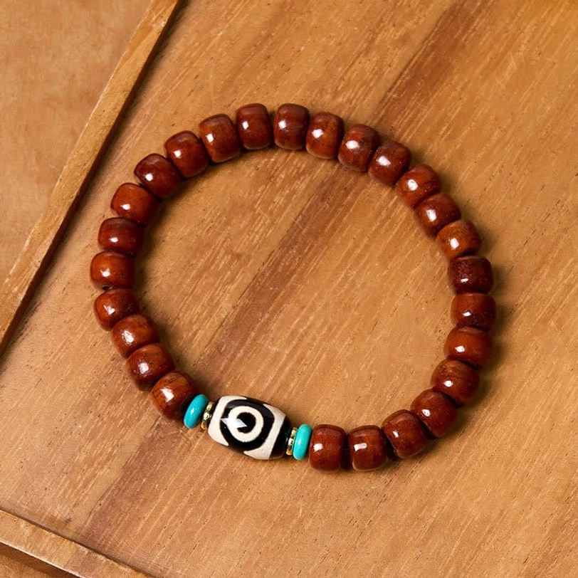 Three-eye Dzi bone luck bracelet with round brown beads and turquoise accents overhead flat lay