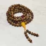108 amber mala beads with yellow guru bead and red spacer beads, displaying full gourd charm pendant on light textured background