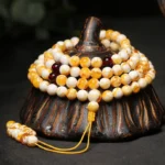 Tibetan 108 amber mala beads necklace with yellow-white marbled beads and dark red spacers displayed on carved wooden base, showing top and side view
