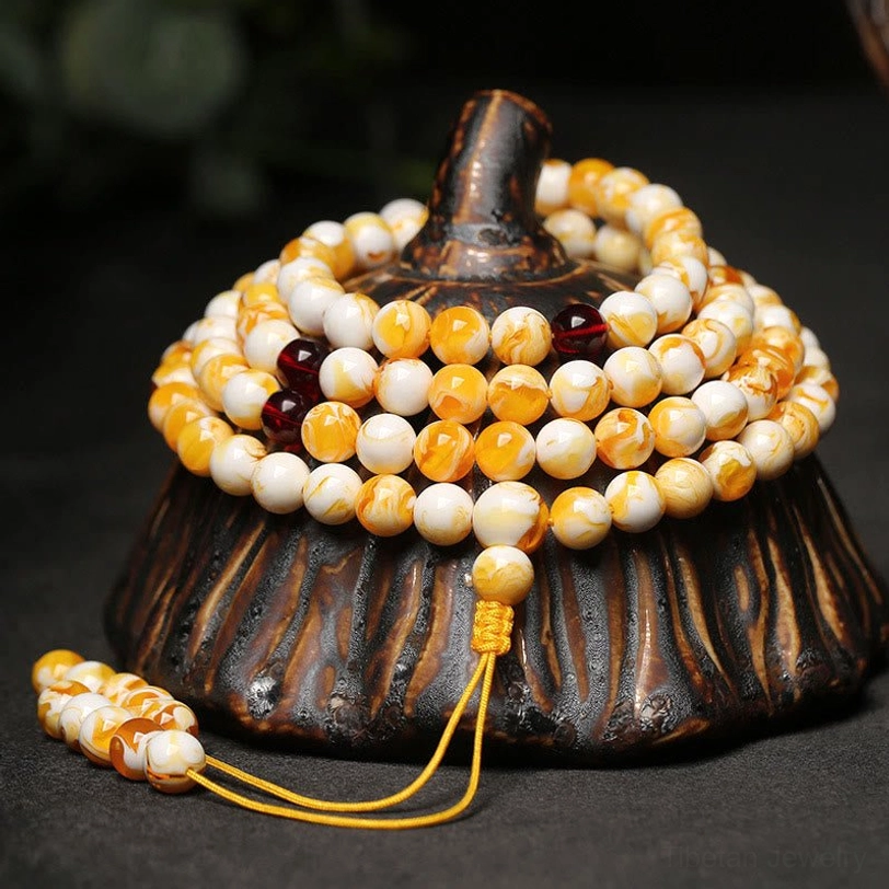 Tibetan 108 amber mala beads necklace with yellow-white marbled beads and dark red spacers displayed on carved wooden base, showing top and side view