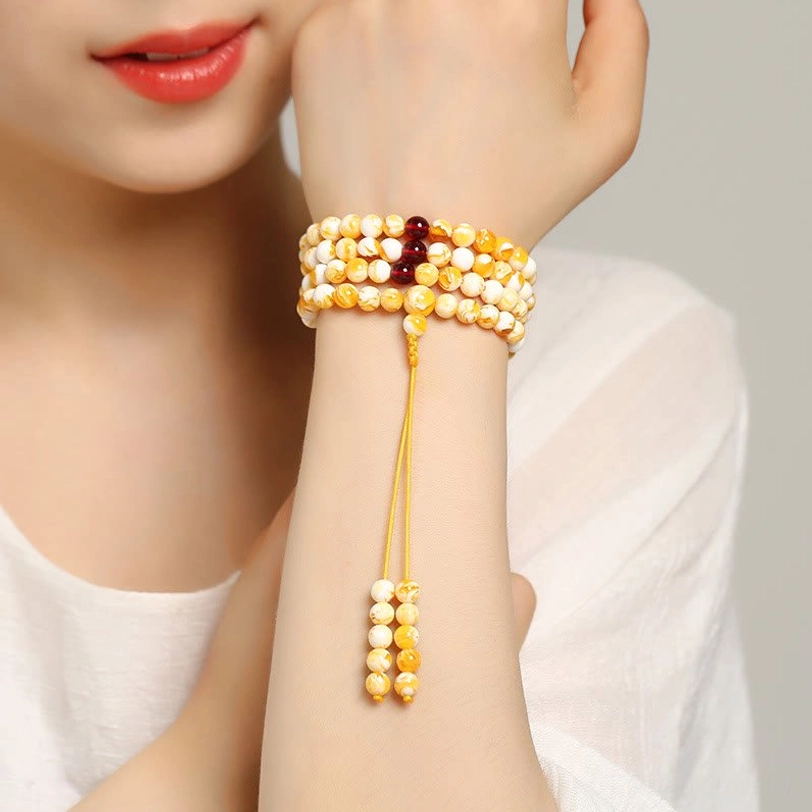 Tibetan amber mala beads showing complete 108-bead string with yellow-white marbled pattern, dark red glass spacers, and golden tassel on white background