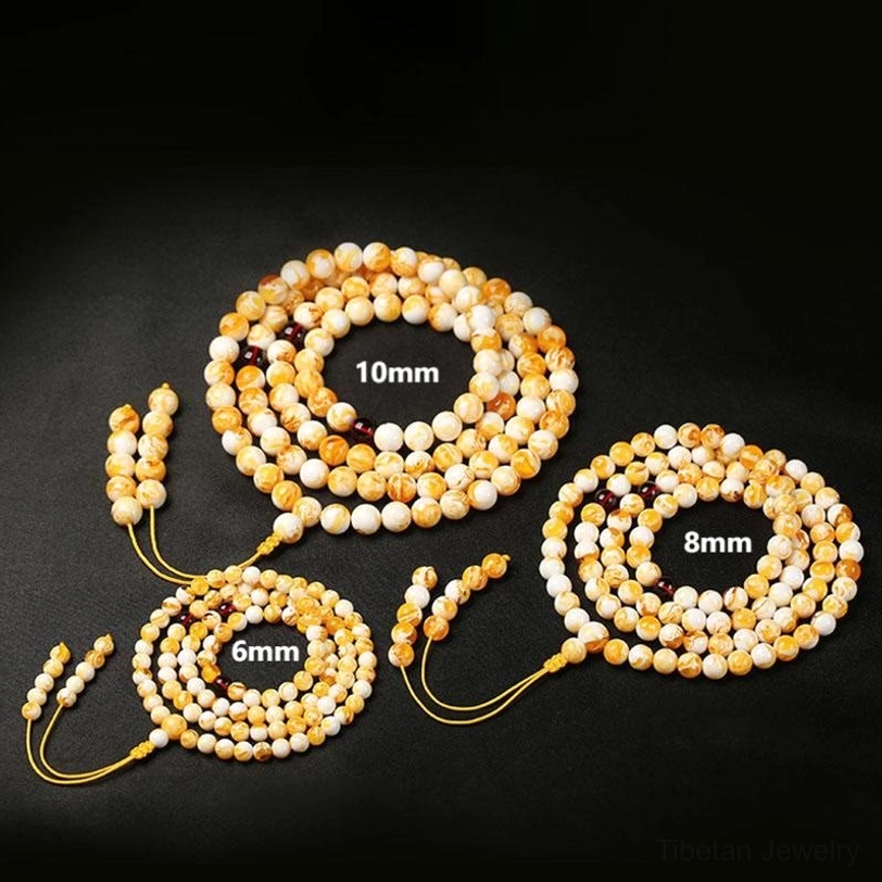 Tibetan 108-bead amber mala necklace featuring marbled golden-yellow and creamy-white beads with dark red spacers and silk tassel