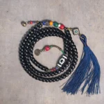 Tibetan 108-bead mala bracelet with ebony wood beads, hand-painted dzi bead, and copper accents featuring blue tassel - top view flat lay