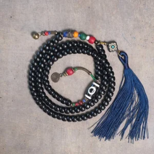 Tibetan 108-bead mala bracelet with ebony wood beads, hand-painted dzi bead, and copper accents featuring blue tassel - top view flat lay