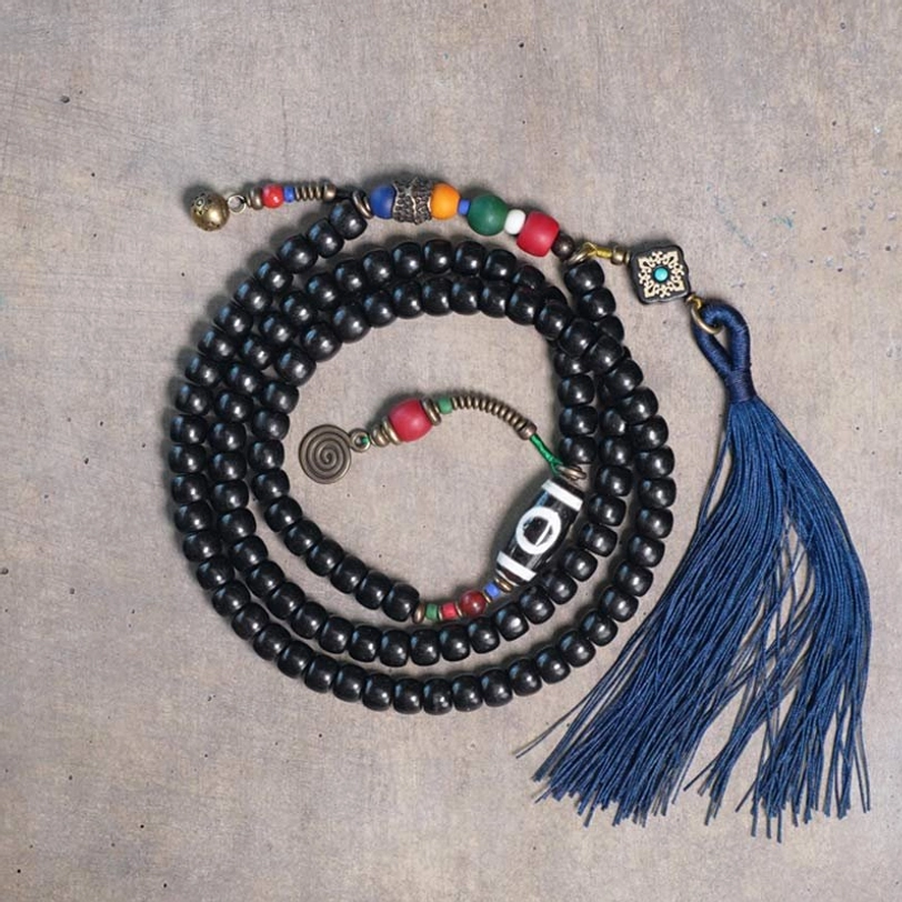 Tibetan 108-bead mala bracelet with ebony wood beads, hand-painted dzi bead, and copper accents featuring blue tassel - top view flat lay