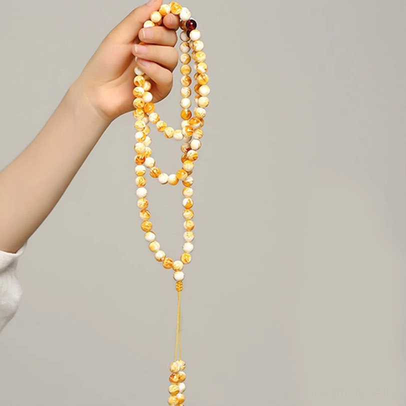 Tibetan 108-bead prayer mala held in human hand, yellow tassel pendant visible, side view against white background