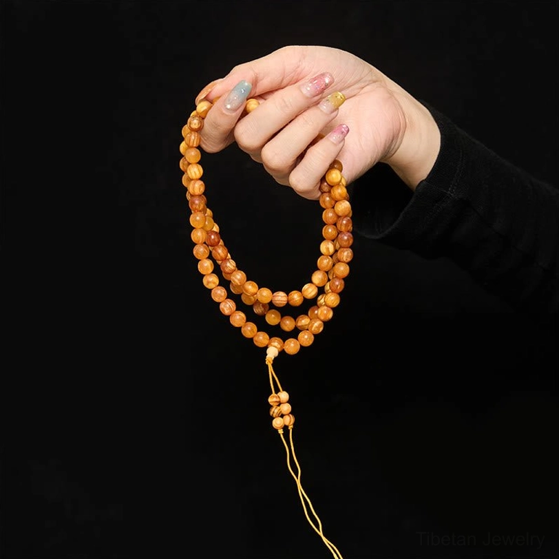 hand holding single-strand 108-bead pine wood mala necklace with decorative tassel shown in studio lighting