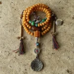 Tibetan 108 bodhi seed mala bracelet with copper Bagua vajra pendant and turquoise accents, flat lay top view on concrete texture
