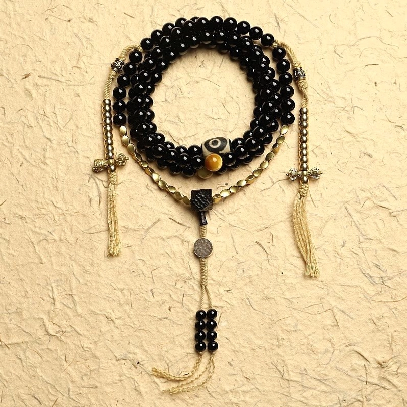 Tibetan 108 mala beads bracelet with black onyx and three-eyed dzi bead displayed in flat lay on textured background