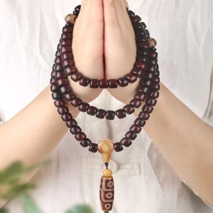 108 mala beads bracelet with three-eye dzi bead held in hand showing deep brown wooden beads, light spacers, and patterned dzi charm