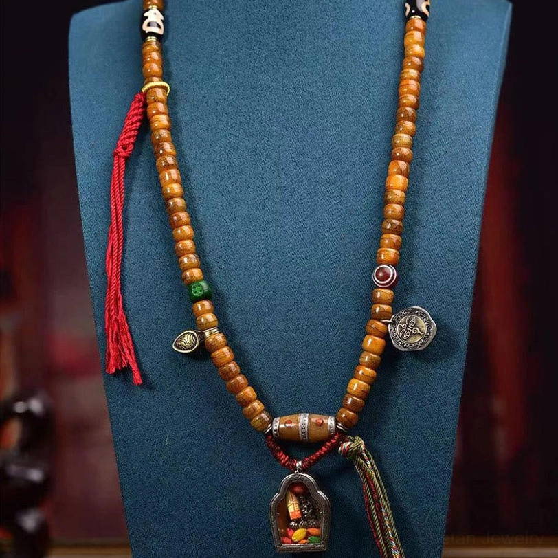 Complete Tibetan 108 mala necklace displayed on blue jewelry stand with tan bone beads, metal charms, and red tassel