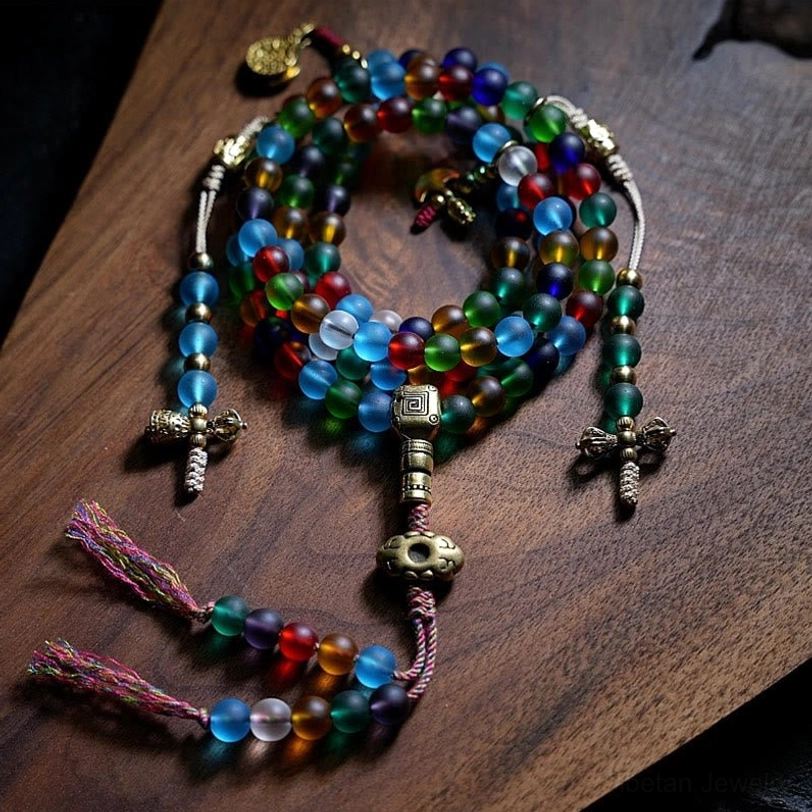 Tibetan 108 mala bead bracelet with multicolored frosted liuli glass beads and brass Bagua charm, overhead flat lay view on dark wood