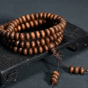 108 wooden mala beads arranged in a circle on dark wooden base - Tibetan prayer necklace with natural wood grain texture and knotted tassel