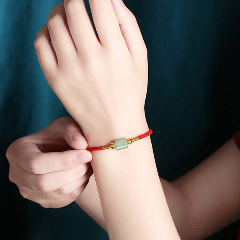 Adjustable Tibetan woven bracelet with red braided rope, light green barrel bead, and gold hardware shown in hand adjustment position