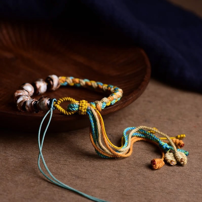 Tibetan handmade adjustable bracelet with knotted braid details and long cord tassels, top-down angled view on dark wooden plate