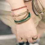 Red agate and brass triple wrap Tibetan bracelet worn on wrist with casual linen outfit, overhead view showing layered design