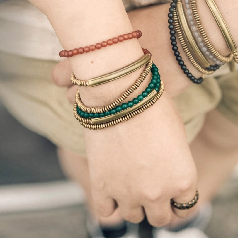 Red agate and brass triple wrap Tibetan bracelet worn on wrist with casual linen outfit, overhead view showing layered design