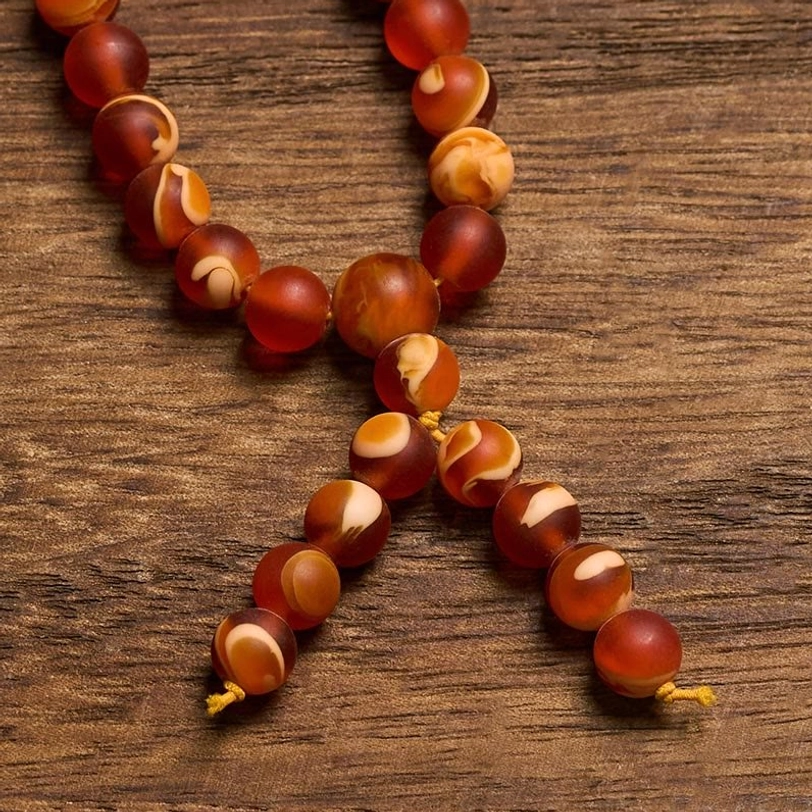 Macro detail of irregular two-tone amber mala beads on wooden background, revealing natural texture and polish of each bead