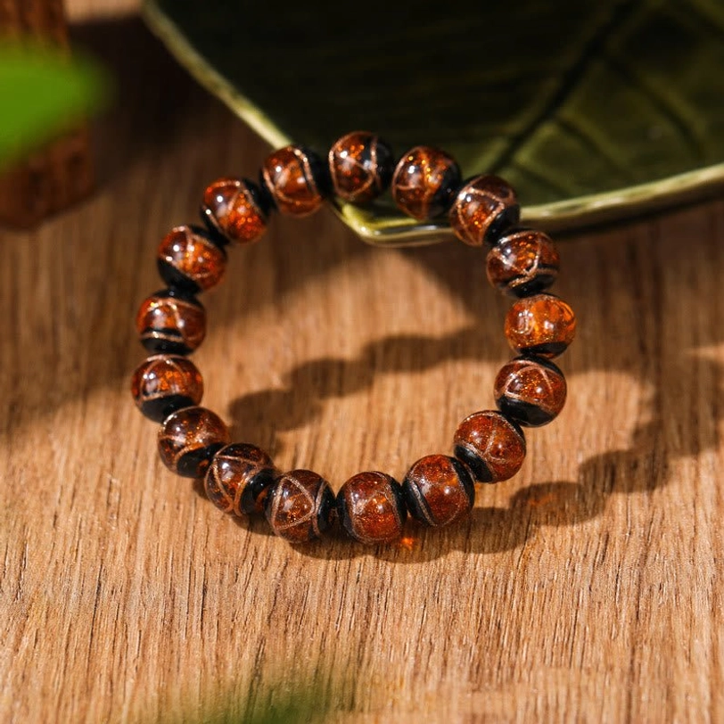 Single amber-brown Tibetan glass beaded bracelet with rich warm brown glossy round classic beads on overhead wooden table display