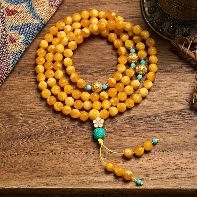 108-bead Tibetan amber mala necklace with turquoise accents and decorative tassel, displayed on ethnic fabric with warm lighting
