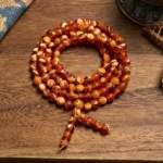108 Tibetan amber mala beads with tassel on wooden surface, top-down view showing warm honey-colored beads and spiritual pendant