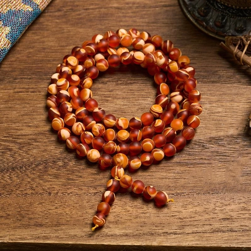 108 Tibetan amber mala beads with tassel on wooden surface, top-down view showing warm honey-colored beads and spiritual pendant