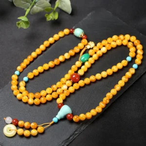 Top-down view of 108-bead Tibetan amber mala with turquoise and red agate accents, peace buckle charm and metal guru bead on dark slate