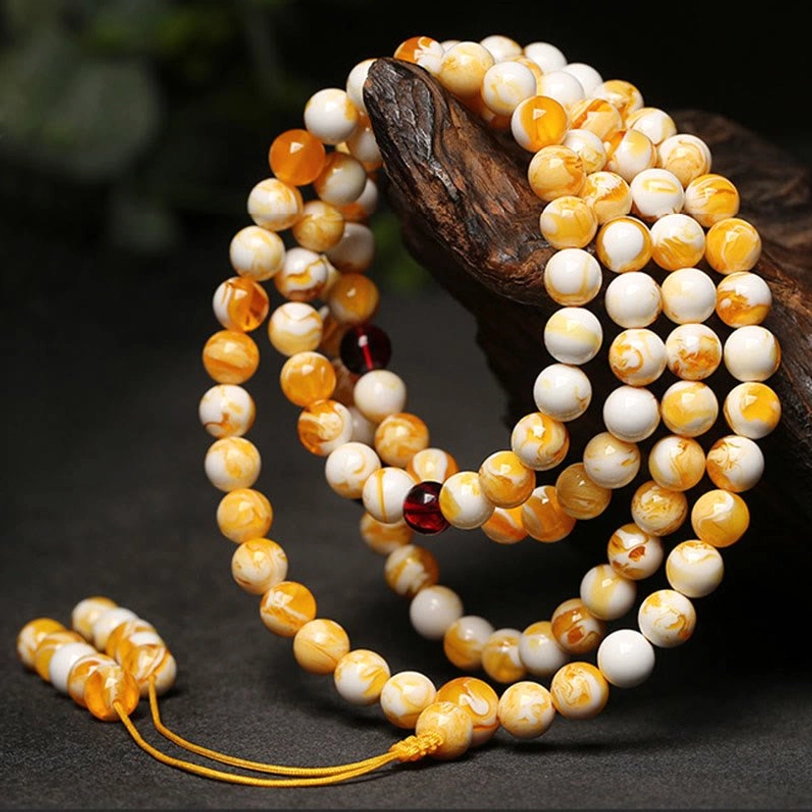 Amber mala beads with marbled yellow-white beads and dark red glass spacers on dark wood surface, oblique overhead angle