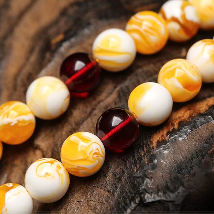 Close-up detail of Tibetan amber mala beads showing marbled yellow-white beads and dark red glass spacer beads on dark wood