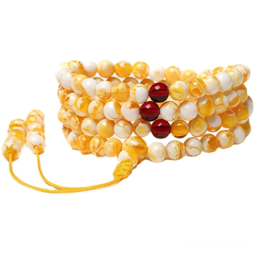 Multiple stacked Tibetan amber mala prayer beads with solid warm yellow beads and yellow tassel counters on black fabric background