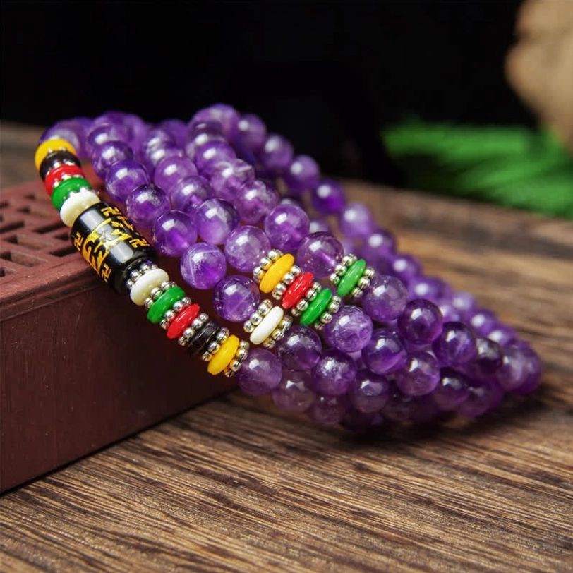 Authentic Tibetan amethyst 108-bead mala with deep purple crystals and colored spacer beads on natural wood table