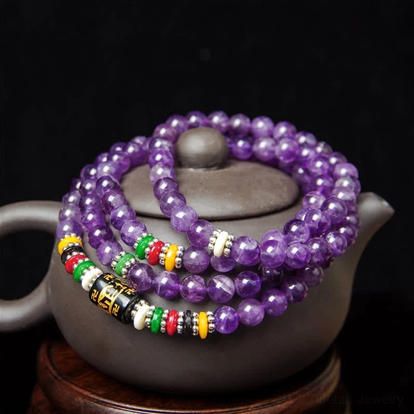 Deep purple amethyst mala with multi-colored spacer beads and mantra ornaments on ceramic teapot
