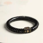 Tibetan coconut shell auspicious clouds bracelet flat lay view featuring black beads and gold engraved metal cloud spacer on neutral background