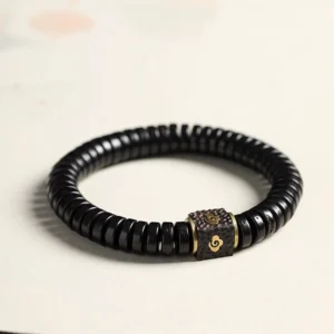 Tibetan coconut shell auspicious clouds bracelet flat lay view featuring black beads and gold engraved metal cloud spacer on neutral background