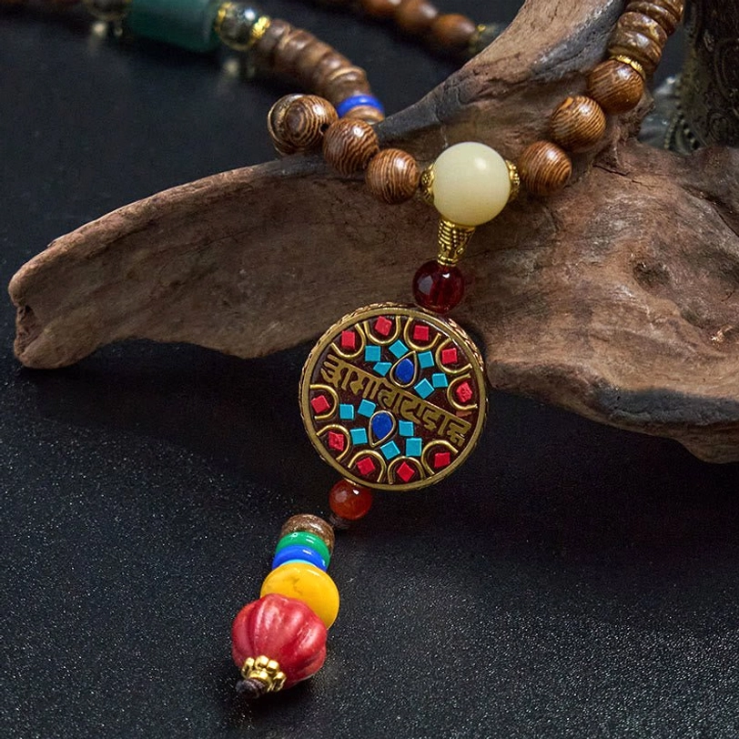 Tibetan Buddhist necklace with brown wooden beads, white accent bead, and enamel mantra pendant on driftwood