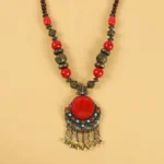 Tibetan beaded hair tassel clip top-down flat lay showing copper metal pendant with red resin center stone and tassel bells