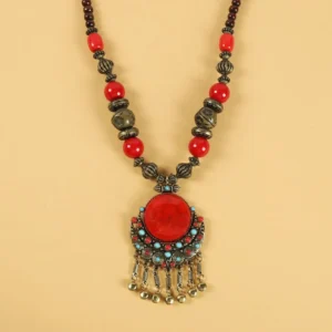 Tibetan beaded hair tassel clip top-down flat lay showing copper metal pendant with red resin center stone and tassel bells