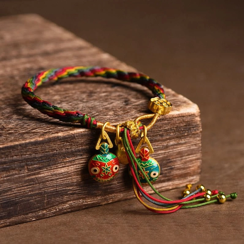 Tibetan gold swallowing beast bracelet close-up side view showing multicolor woven cord enamel pendants and beaded gold tassel