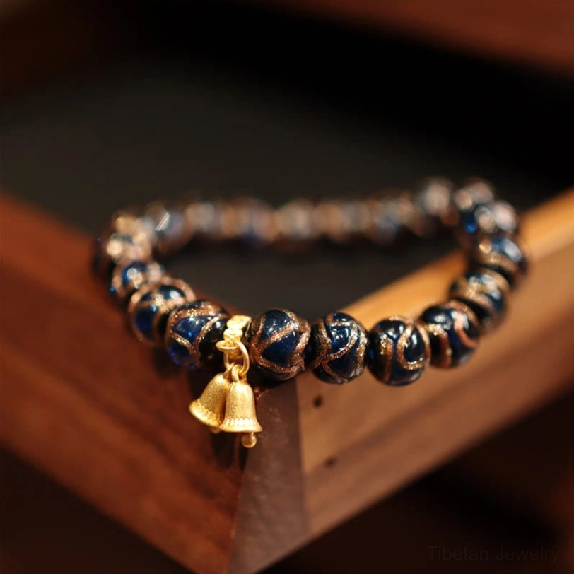 Tibetan style bell charm bracelet with dark glossy stone beads and gold bell pendant on wooden tray