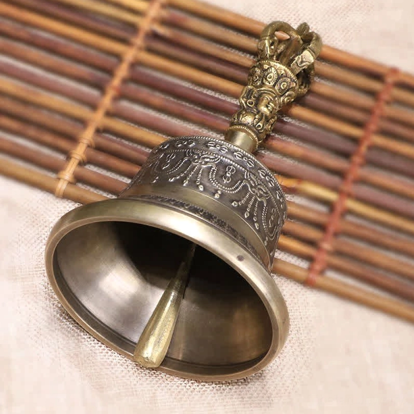 Low angle close-up of Tibetan meditation bell showing internal clapper and carved handle detail in aged bronze tone