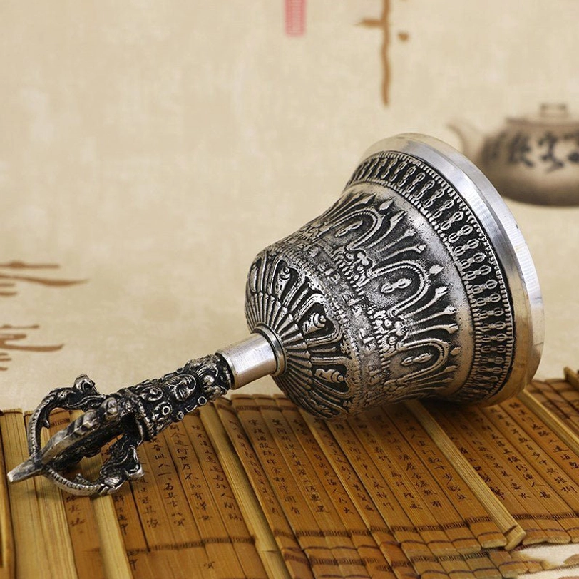 Tibetan bell and vajra dorje side view on bamboo slip calligraphy background, aged silver finish with detailed carved religious motifs visible