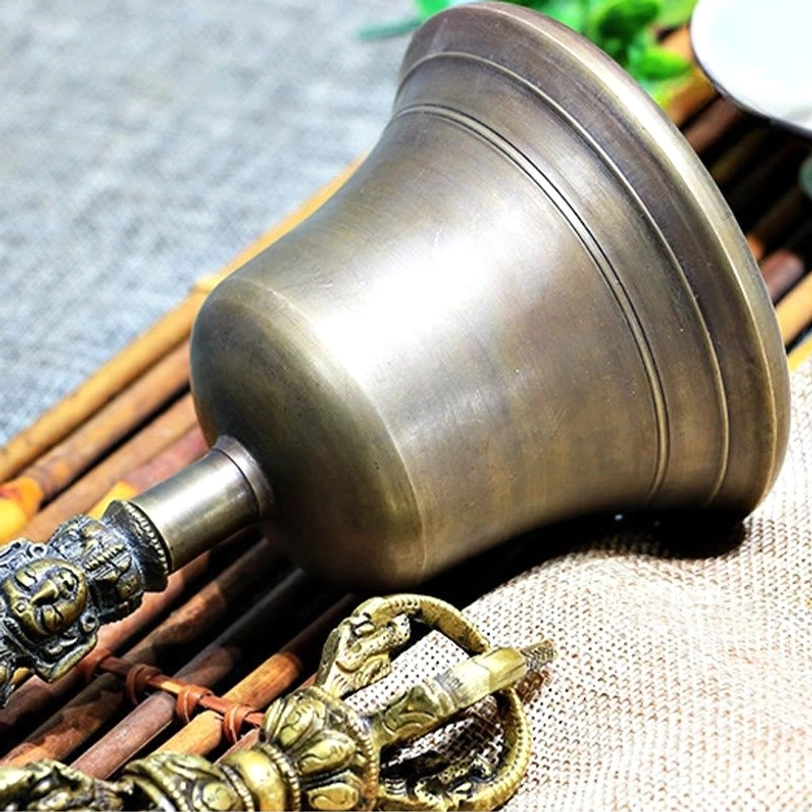 Close-up detail of Tibetan meditation bell handle with carved deity face and ornate bronze copper patterns