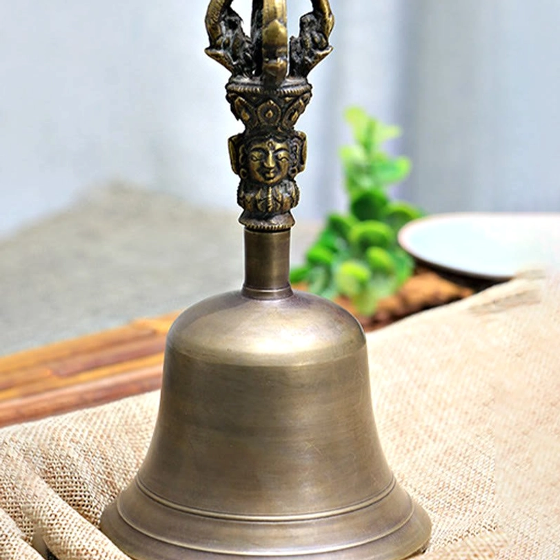 Polished bronze copper Tibetan meditation bell with smooth rounded body, overhead view on bamboo mat with green decor