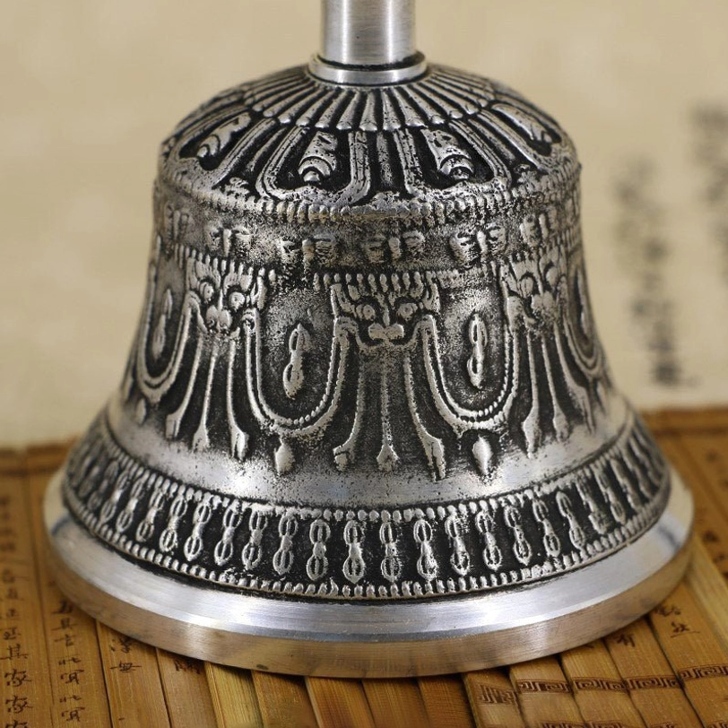 Close-up detail of Tibetan meditation bell showing relief carvings on bell body and polished copper metal base on bamboo slip background