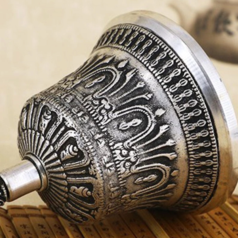Low-angle side close-up of handcrafted Tibetan meditation bell showing complex engraved religious patterns and aged silver tone on bamboo background